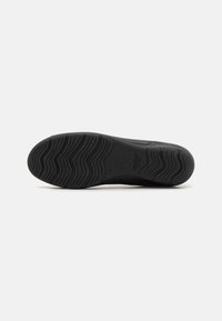Suela de zapato de goma negra con diseño de banda de rodadura ondulada, marca embosada y bordes suaves; presenta un material duradero para tracción y soporte.
