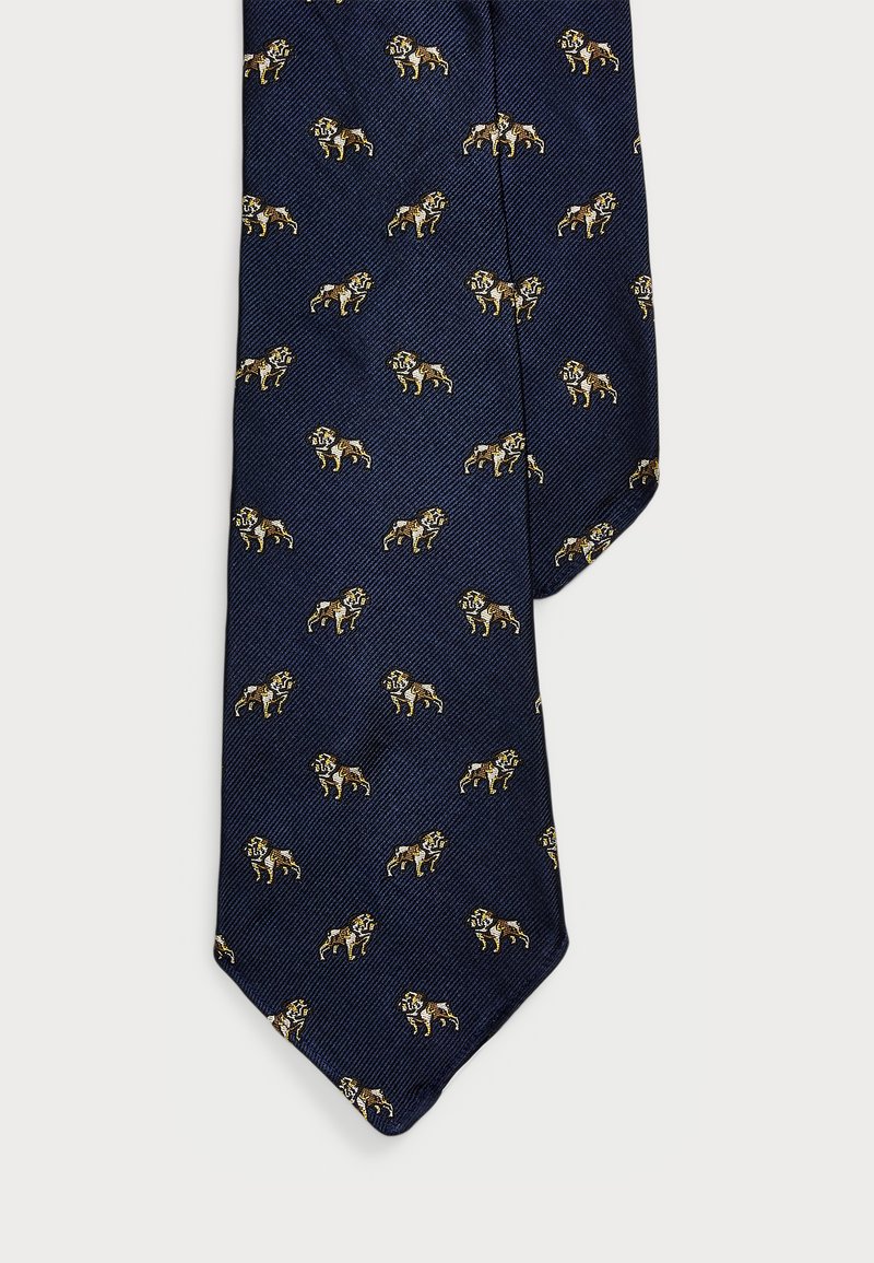 Sötét háttérrel rendelkező, textúrált anyagból készült tengerészkék nyakkendő, amelyen arany és barna árnyalatú, ismétlődő oroszlán minta található.