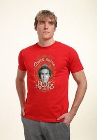 Czerwona bawełniana koszulka z centralnym nadrukiem zawierającym napis "I AM A COTTON-HEADED NINNY MUGGINS" oraz ilustracją twarzy.