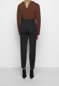 Maglione marrone a maglia, pantaloni neri su misura e stivali alla caviglia neri. L'insieme presenta un maglione testurizzato e un design elegante dei pantaloni con tasche.