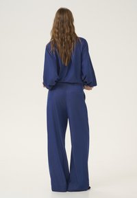 Modrý dvoudílný outfit s volným topem a kalhotami širokého střihu, s jemnou texturou, dlouhými rukávy a čistým, minimalistickým designem.