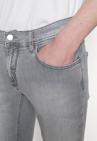 Jeans de mezclilla gris con un corte ajustado, diseño de cinco bolsillos y un cierre de botón plateado en la cintura, con un ligero desgaste en toda su superficie.