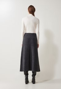 Falda larga de color gris oscuro con una cinturilla acanalada, hecha de una tela suave. Combinada con una blusa ajustada de manga larga clara y botas negras hasta la rodilla.