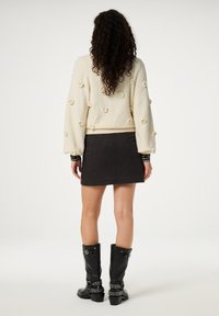 Crème gebreid sweater met bloemapplicaties, gecombineerd met een zwarte minirok met een textuurpatroon. Zwarte leren kniehoge laarzen met studs.
