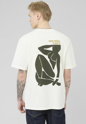 Jeune homme tatoué portant un T-shirt blanc avec au dos une figure féminine abstraite noire "Nu Bleu III" de Henri Matisse.