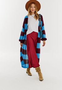 Wielokolorowy, dziergany kardigan w niebieskie i bordowe paski, z długimi rękawami, noszony na białej bluzce i czerwonej spódnicy, zestawiony z beżowymi botkami.