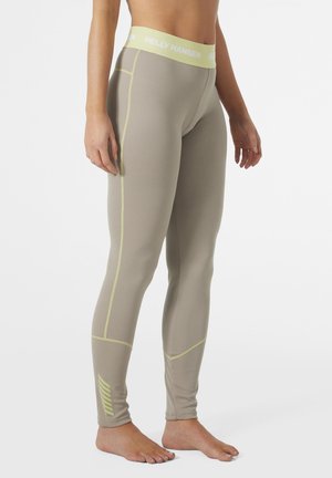 Leggings de color beige claro con un acabado texturizado, que presentan costuras y acentos en color amarillo lima, y una cintura con logo. Diseño ajustado, de largo hasta el tobillo.