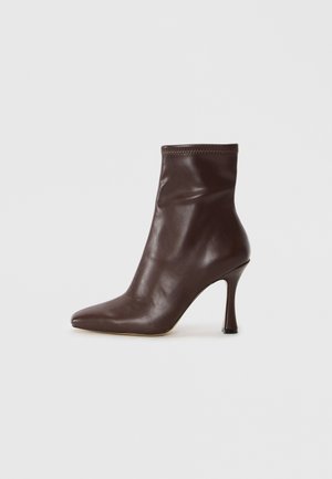 Stivaletto in pelle marrone con punta affusolata e tacco a stiletto sottile. Presenta una texture liscia e dettagli cuciti attorno all'apertura.