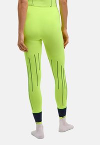 Legginsy neonowożółte z czarnymi pionowymi paskami, o dopasowanym kroju, prążkowanej fakturze i ciemnoniebieskich mankietach przy kostkach, przeznaczone do noszenia sportowego.