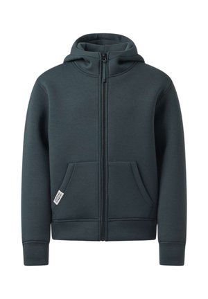 Garçon debout, main sur la nuque, portant un sweat à capuche zippé foncé, un jean bleu clair et des baskets blanches avec des rayures noires.