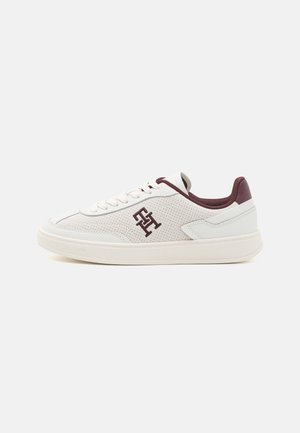 Baskets basses blanches avec côtés perforés, doublure bordeaux, lacets et monogramme brodé bordeaux sur une semelle blanche.