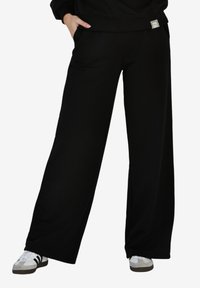 Czarne szerokie spodnie dresowe wykonane z miękkiego materiału, z bocznymi kieszeniami i subtelnym, wzorzystym akcentem na pasku.