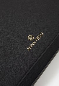 Svart texturerad läderanteckningsbok med guldprägling av "ANNA FIELD"-logotypen och ett cirkulärt blommönster som detalj. Släta kanter och minimalistisk design.