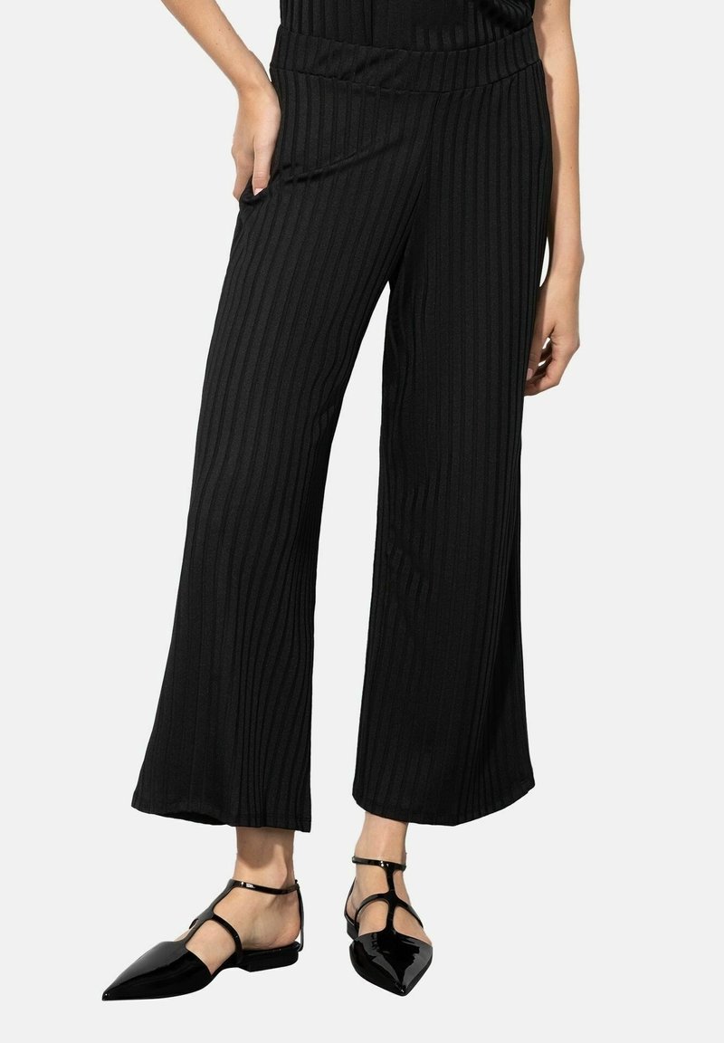 Un pantalon large noir côtelé avec une taille haute et des poches latérales. Assorti à des ballerines noires à bout pointu avec des brides à la cheville.
