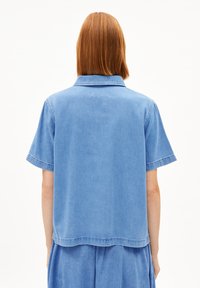 Blaues Denim-Hemd mit kurzen Ärmeln und Kragen, mit einem lässigen Schnitt und geradem Saum. Der Stoff hat eine glatte Textur und einen dezenten Glanz.