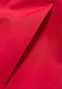 Tessuto rosso che mostra una superficie liscia e satinata con lucentezza. Presenta una piega diagonale, che indica un design a strati. Nessun motivo o dettaglio distintivo.