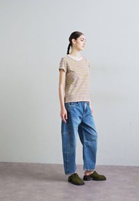 Riba t-särk ümmarguse kaelusega, sinised laiad teksad ja oliivrohelised puukingad paksu tallaga. Minimalistlik disain, mugav lõige.