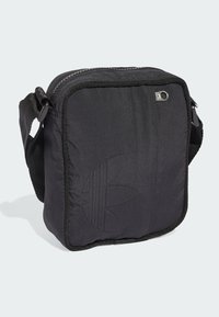 Bolso crossbody de tela negra con cierre de cremallera, que presenta un logo en relieve, superficie texturizada y una correa ajustable.