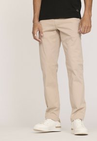 Pantalon en coton beige à coupe droite, avec une texture lisse et des coutures minimales, associé à des baskets blanches.