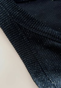 Nærbillede af foldet mørkeblå strikket stof med sølvmetaltråde, der skaber en subtil glimtende effekt.