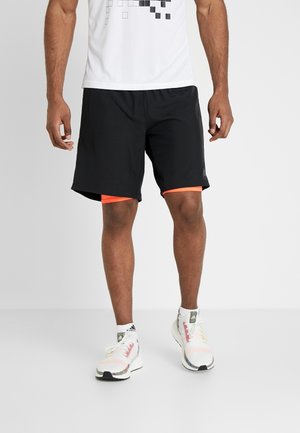 Czarne sportowe szorty z pomarańczową lamówką, noszone z białą koszulką z nadrukiem oraz kolorowymi butami sportowymi z fakturowaną cholewką i białymi sznurowadłami.