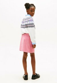 Witte gebreide trui met een patroon op de schouders, gecombineerd met een roze corduroy rok. Zwarte schoenen maken de outfit compleet.