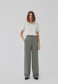 Light beige short-sleeve t-shirt, paired with high-waisted, wide-leg olive green trousers. Trousers feature front pockets and button closure.