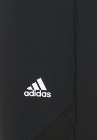 Mustat urheilulegginsit, jotka on valmistettu venyvästä materiaalista. Niissä on verkkopaneelit ja valkoinen Adidas-logo lähellä alaosaa.