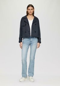 Marineblauwe cropped dubbelzijdige jas met grote knopen, gecombineerd met lichtblauwe flared jeans en witte platform sneakers.
