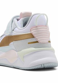 Sportssko med en vit mesh-övre, guld- och silverdetaljer, rosa detaljer på hälen och en texturerad gummisula med en ljus pastellfärgskala.