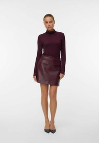 Bordo odinė sijonas su dviem kišenėmis, derinamas su prigludusia, ilgomis rankovėmis tamsia blusa. Modelis vilki smailius juodus batelius su baltais akcentais.