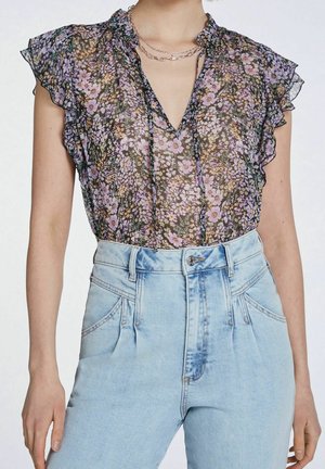 Blouse noire transparente à imprimé floral violet avec manches volantées, rentrée dans un jean en denim bleu clair taille haute à plis.