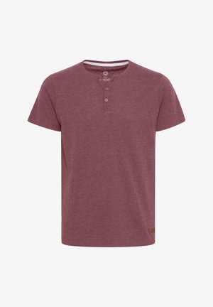 Kortermet, bordeaux T-skjorte laget av mykt stoff. Har rund hals med tre knapper og en liten brun etikett på kanten.