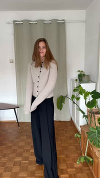 Beige ribbad kavaj med svarta knappar, tillsammans med löst sittande svarta byxor. Ljus träfärg på golvet och inomhusväxter i bakgrunden.