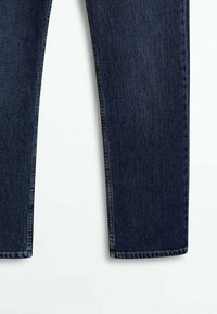 Jambes de jeans en denim bleu foncé, présentées à plat sur fond blanc, coupe droite avec coutures visibles aux ourlets et aux coutures.