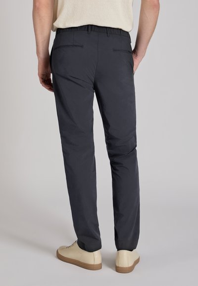 Navy blue trousers featuring an elastic waistband, two back pockets, and a slim fit design, paired with beige sneakers.