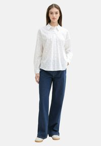 Weißes Hemd mit strukturierten Pünktchen, kombiniert mit blauen weiten Jeans und hellen Schuhen.