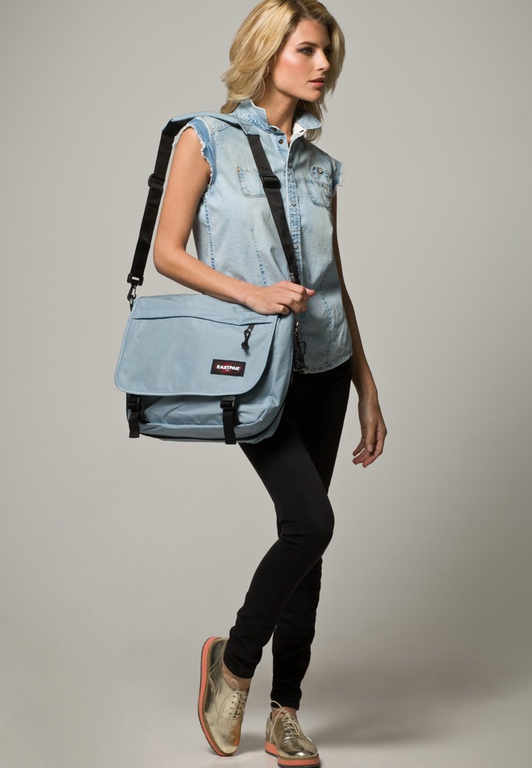 Bolso mensajero de color azul claro, hecho de tela duradera, cuenta con un cierre a presión con hebillas y un bolsillo con cremallera en la parte frontal, se lleva cruzado.
