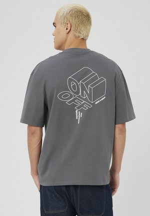 T-shirt en coton gris avec un graphisme au dos comportant les mots "ON" et "OFF" en lettres grasses et contournées, ainsi qu'un texte supplémentaire en dessous.