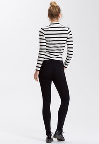 Czarne, dopasowane jeansy wąskie w połączeniu z czarno-białą, paskowaną bluzką z długim rękawem. Ma okrągły dekolt i prążkowaną fakturę.