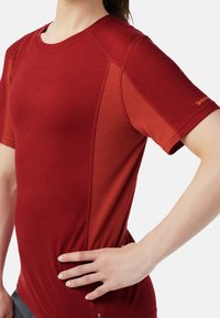 Red athletic shirt with short sleeves, featuring a solid body and textured side panels. The fabric appears lightweight with a smooth finish.