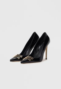 Μαύρα ψηλά τακούνια από λουστρίνι με μυτερή μύτη, χρυσές μεταλλικές λεπτομέρειες και λεπτό στιλέτο τακούνι. Ομαλή υφή και κομψός σχεδιασμός.