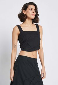 Črn skrajšan top s kvadratnim izrezi, širokimi naramnicami in teksturiranim aplikacijskim detajlom. Pairs with a matching black high-waisted skirt.
