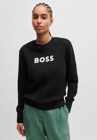 Black sweatshirt featuring a prominent white "BOSS" logo on the front. Made of soft fabric with a crew neck and ribbed cuffs.