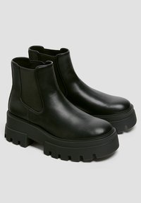 Bottes noires en cuir avec panneaux latéraux élastiques, semelles en caoutchouc épaisses, bouts arrondis et finition lisse. Design robuste et surélevé.