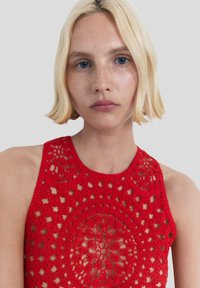 Red crochet tank top featuring intricate patterns and open-knit design with circular motifs. Textured fabric and sleeveless style.