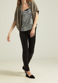 Za duży beżowy kardigan na czarno-białej wzorzystej bluzce, zestawiony z czarnymi dopasowanymi spodniami i czarnymi spiczastymi balerinami.