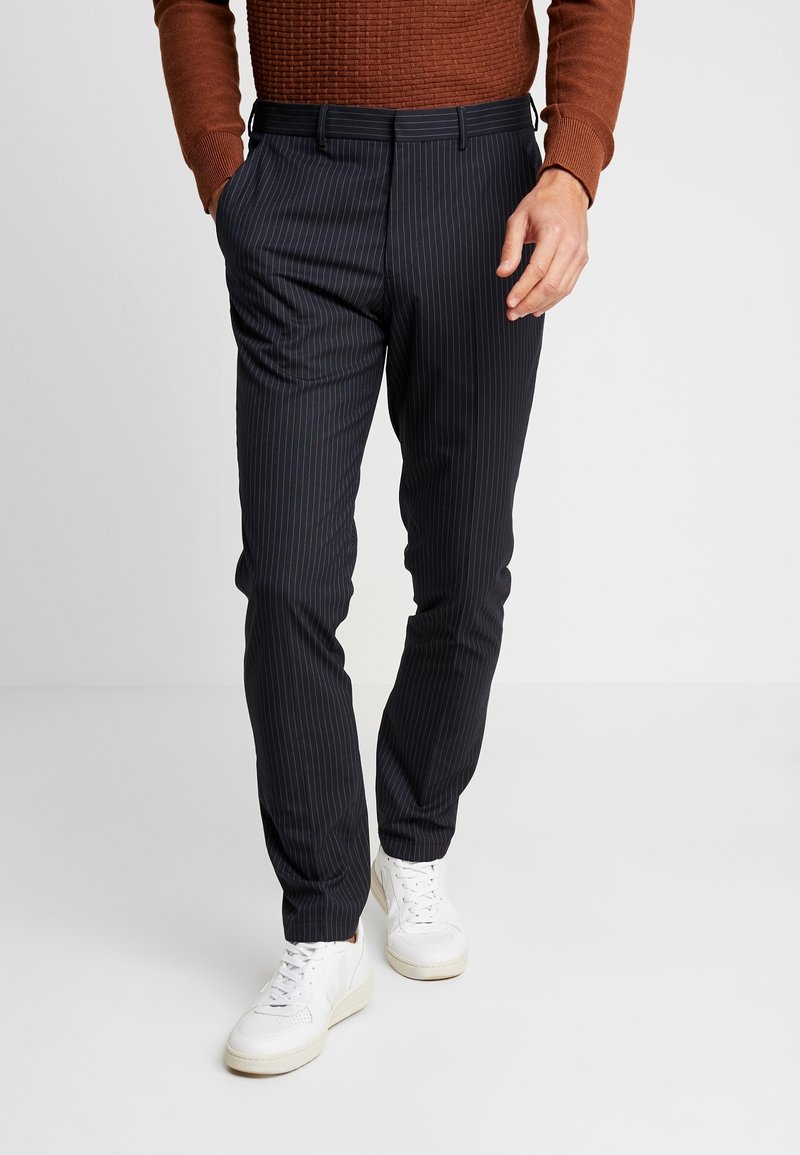 Ränderbyxor i mörk marinblått tyg, slim fit, med sidfickor och bälteshällor, i kombination med vita sneakers.