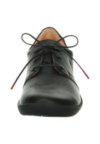 Chaussure en cuir noir à lacets avec un bout arrondi, semelle plate et lacets aux extrémités rouges. Elle présente une texture lisse et un design minimaliste.