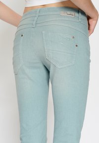 Jasnoniebieskie dżinsy z gładką fakturą. Posiadają dwie tylne kieszenie i ozdobne przeszycia, podkreślone małymi metalowymi ćwiekami.